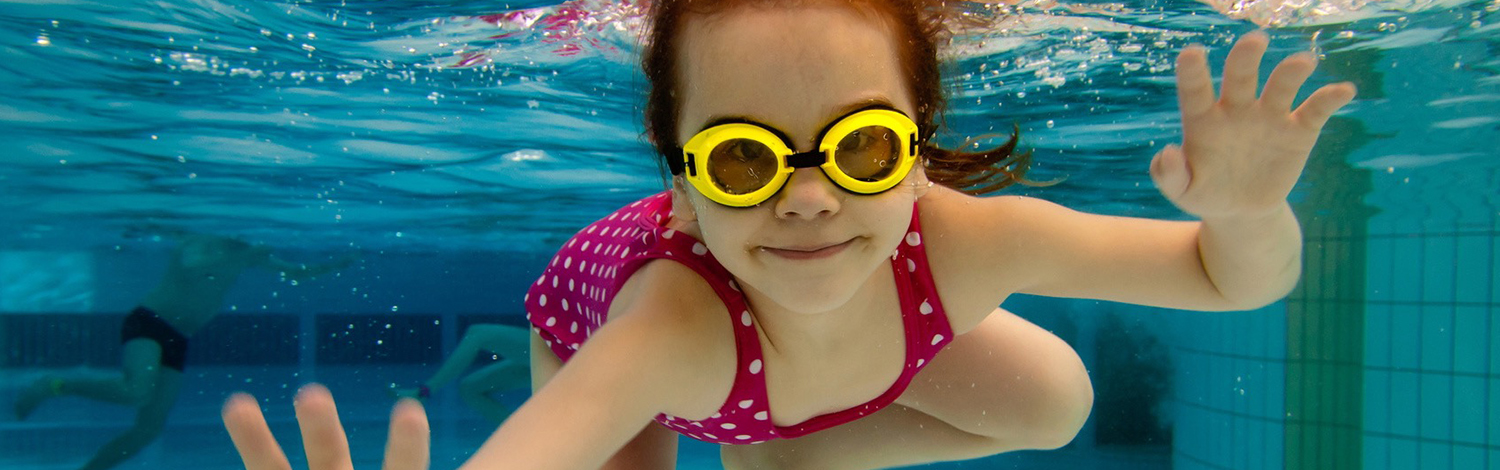 girl with goggles swimming under water in pool